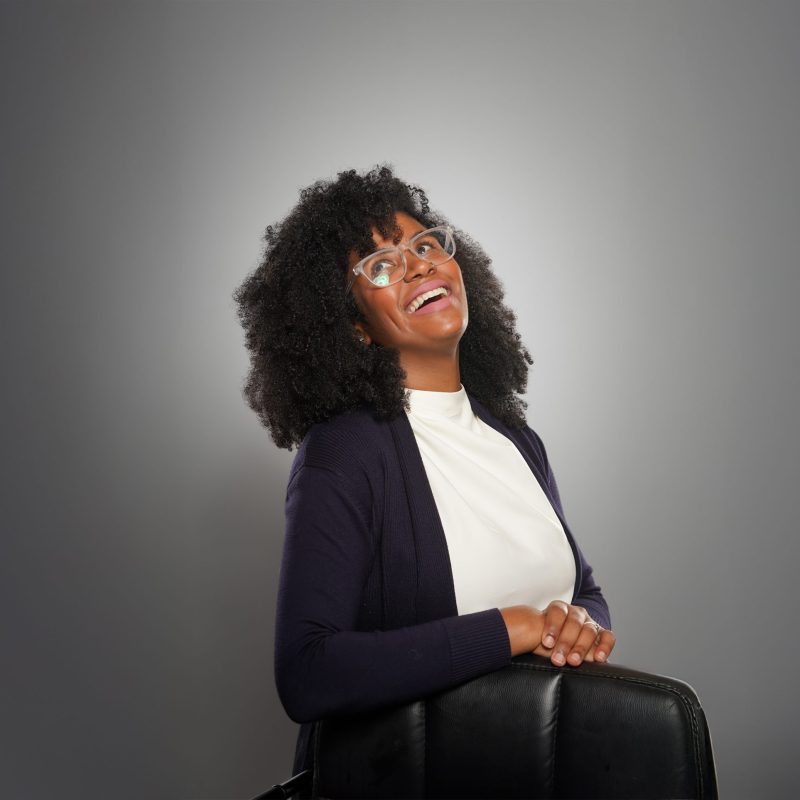 Smiling woman with curly hair and glasses against gray background